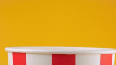 Patlamış mısır taneleri şeftali arka planda izole edilmiş kırmızı ve beyaz çizgili kovaya düşer. Atıştırmalık film, fast food kafe tatlı aperatif. Yavaş çekim.