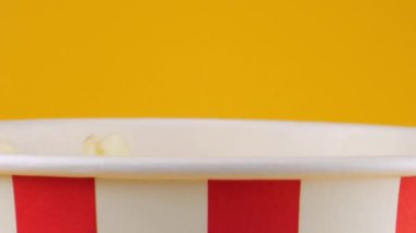 Patlamış mısır taneleri şeftali arka planda izole edilmiş kırmızı ve beyaz çizgili kovaya düşer. Atıştırmalık film, fast food kafe tatlı aperatif. Yavaş çekim.