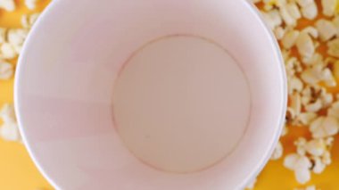 Patlamış mısır taneleri şeftali arka planda izole edilmiş kırmızı ve beyaz çizgili kovaya düşer. Atıştırmalık film, fast food kafe tatlı aperatif. Üst Manzara. Yavaş çekim.