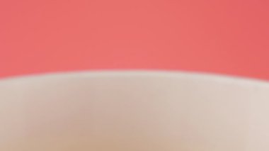 Patlamış mısır taneleri pembe arka planda izole edilmiş kırmızı ve beyaz çizgili kovaya düşer. Atıştırmalık film, fast food kafe tatlı aperatif. Yavaş çekim.