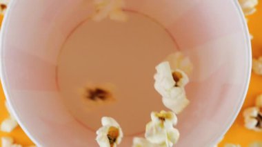 Patlamış mısır taneleri şeftali arka planda izole edilmiş kırmızı ve beyaz çizgili kovaya düşer. Atıştırmalık film, fast food kafe tatlı aperatif. Üst Manzara. Yavaş çekim.