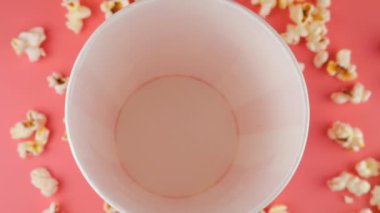 Patlamış mısır taneleri pembe arka planda izole edilmiş kırmızı ve beyaz çizgili kovaya düşer. Atıştırmalık film, fast food kafe tatlı aperatif. Üst Manzara. Yavaş çekim.