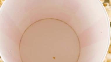 Patlamış mısır taneleri arka plandaki patlamış mısır tanelerinin üzerine kırmızı ve beyaz çizgili kovaya düşüyor. Atıştırmalık film, fast food kafe tatlı aperatif. Yavaş çekim.