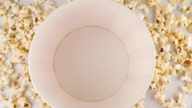 Patlamış mısır taneleri beyaz arka planda izole edilmiş kırmızı ve beyaz çizgili kovaya düşüyor. Atıştırmalık film, fast food kafe tatlı aperatif. Ağır çekim. Üst görünüm.