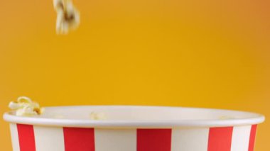 Patlamış mısır taneleri şeftali arka planda izole edilmiş kırmızı ve beyaz çizgili kovaya düşer. Atıştırmalık film, fast food kafe tatlı aperatif. Yavaş çekim.