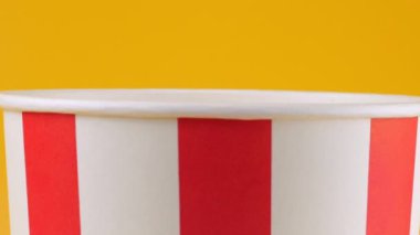 Patlamış mısır taneleri şeftali arka planda izole edilmiş kırmızı ve beyaz çizgili kovaya düşer. Atıştırmalık film, fast food kafe tatlı aperatif. Yavaş çekim.
