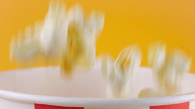 Patlamış mısır taneleri şeftali arka planda izole edilmiş kırmızı ve beyaz çizgili kovaya düşer. Atıştırmalık film, fast food kafe tatlı aperatif. Yavaş çekim.