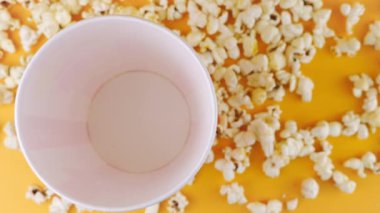 Patlamış mısır taneleri şeftali arka planda izole edilmiş kırmızı ve beyaz çizgili kovaya düşer. Atıştırmalık film, fast food kafe tatlı aperatif. Üst Manzara. Yavaş çekim.