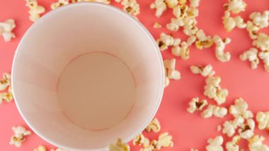 Patlamış mısır taneleri pembe arka planda izole edilmiş kırmızı ve beyaz çizgili kovaya düşer. Atıştırmalık film, fast food kafe tatlı aperatif. Üst Manzara. Yavaş çekim.