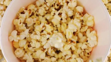 Patlamış mısır taneleri arka plandaki patlamış mısır tanelerinin üzerine kırmızı ve beyaz çizgili kovaya düşüyor. Atıştırmalık film, fast food kafe tatlı aperatif. Ağır çekim. Üst görünüm.