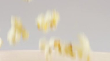 Patlamış mısır taneleri beyaz arka planda izole edilmiş kırmızı ve beyaz çizgili kovaya düşüyor. Atıştırmalık film, fast food kafe tatlı aperatif. Yavaş çekim.