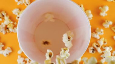 Patlamış mısır taneleri şeftali arka planda izole edilmiş kırmızı ve beyaz çizgili kovaya düşer. Atıştırmalık film, fast food kafe tatlı aperatif. Üst Manzara. Yavaş çekim.