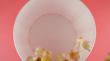 Patlamış mısır taneleri pembe arka planda izole edilmiş kırmızı ve beyaz çizgili kovaya düşer. Atıştırmalık film, fast food kafe tatlı aperatif. Üst Manzara. Yavaş çekim.