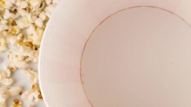 Patlamış mısır taneleri beyaz arka planda izole edilmiş kırmızı ve beyaz çizgili kovaya düşüyor. Atıştırmalık film, fast food kafe tatlı aperatif. Ağır çekim. Üst görünüm.
