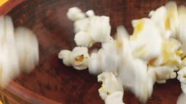 Patlamış mısır taneleri şeftali arka planında izole bir şekilde kahverengi kil kaseye düşüyor. Ağır çekim. Atıştırmalık film, fast food kafe tatlı aperatif.