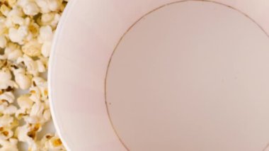 Patlamış mısır taneleri arka plandaki patlamış mısır tanelerinin üzerine kırmızı ve beyaz çizgili kovaya düşüyor. Atıştırmalık film, fast food kafe tatlı aperatif. Yavaş çekim.