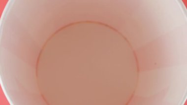 Patlamış mısır taneleri pembe arka planda izole edilmiş kırmızı ve beyaz çizgili kovaya düşer. Atıştırmalık film, fast food kafe tatlı aperatif. Üst Manzara. Yavaş çekim.