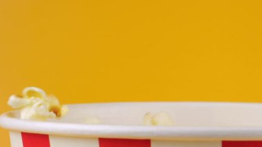 Patlamış mısır taneleri şeftali arka planda izole edilmiş kırmızı ve beyaz çizgili kovaya düşer. Atıştırmalık film, fast food kafe tatlı aperatif. Yavaş çekim.
