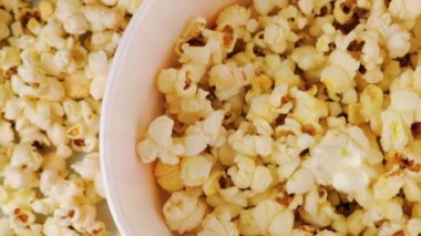 Patlamış mısır taneleri arka plandaki patlamış mısır tanelerinin üzerine kırmızı ve beyaz çizgili kovaya düşüyor. Atıştırmalık film, fast food kafe tatlı aperatif. Ağır çekim. Üst görünüm.