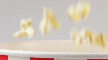 Patlamış mısır taneleri beyaz arka planda izole edilmiş kırmızı ve beyaz çizgili kovaya düşüyor. Atıştırmalık film, fast food kafe tatlı aperatif. Yavaş çekim.