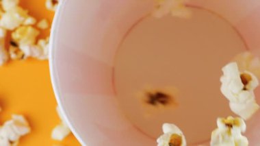 Patlamış mısır taneleri şeftali arka planda izole edilmiş kırmızı ve beyaz çizgili kovaya düşer. Atıştırmalık film, fast food kafe tatlı aperatif. Üst Manzara. Yavaş çekim.