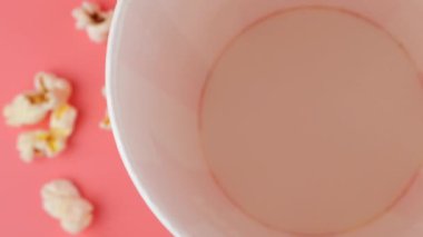 Patlamış mısır taneleri pembe arka planda izole edilmiş kırmızı ve beyaz çizgili kovaya düşer. Atıştırmalık film, fast food kafe tatlı aperatif. Üst Manzara. Yavaş çekim.