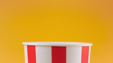 Patlamış mısır taneleri şeftali arka planda izole edilmiş kırmızı ve beyaz çizgili kovaya düşer. Atıştırmalık film, fast food kafe tatlı aperatif. Yavaş çekim.