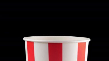 Patlamış mısır taneleri kırmızı ve beyaz çizgili kovaya düşer. Atıştırmalık film, fast food kafe tatlı aperatif. Ağır çekim. Alfa kanalı dahil.