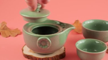Pembe arka planda çay yaprakları olan bir gaiwan 'a sıcak su dökmek. Doğu Asya tarzı çay töreni.