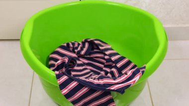 Parlak renkli kadın kıyafetleri plastik bir çamaşır leğenine atılır. Çamaşır yıkama, kıyafet düzenleme ve evi temizleme teması..
