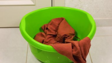 Gri-kahverengi tonlarda kadın kıyafetleri plastik bir çamaşır leğenine atılır. Çamaşır yıkama, kıyafet düzenleme ve evi temizleme teması..