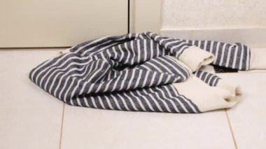 Kiremit zemine örülmüş kazaklar, eşarplar, gri-mavi tonlarda yün şapkalar atılıyor. Çamaşır yıkama, kıyafet düzenleme ve evi temizleme teması..