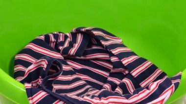 Parlak renkli kadın kıyafetleri plastik bir çamaşır leğenine atılır. Çamaşır yıkama, kıyafet düzenleme ve evi temizleme teması..