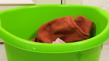 Gri-kahverengi tonlarda kadın kıyafetleri plastik bir çamaşır leğenine atılır. Çamaşır yıkama, kıyafet düzenleme ve evi temizleme teması..