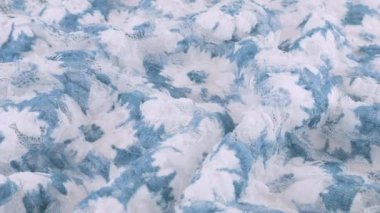 Hafif desenli dantel kumaşın beyaz ve mavi tonlarda kıvrımları ve çiçek desenleri vitrinde dönüyor. Tekstil arka planının üst görüntüsü. Tema tasarımı, moda, kıyafet terziliği.