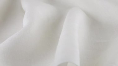 Beyaz keten kumaşın yumuşak kıvrımları vitrinde dönüyor. Tekstil arka planının yakın görüntüsü. Tema tasarımı, moda, kıyafet terziliği.