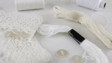 Beyaz keten kumaş, el dokuma danteli, düğmeler, iğne, pamuk iplik makaraları, diş ipi ve iplik. Tekstil arkaplanı görüntüleme kutusunda döner.