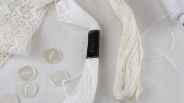 Beyaz keten kumaş, el dokuma danteli, düğmeler, iğne, pamuk iplik makaraları, diş ipi ve iplik. Tekstil arkaplanı görüntüleme kutusunda döner.