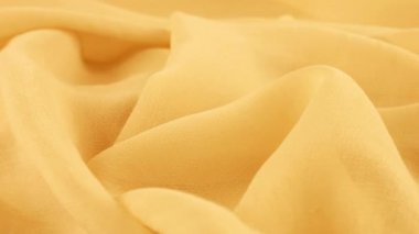 Dönen bir vitrin üzerindeki ince, açık sepya sarısı şifon kumaşının yumuşak kıvrımlarının yakın görüntüsü. Moda, tasarım, kumaş teması üzerine aksesuar dikebilen tekstil arka planı.