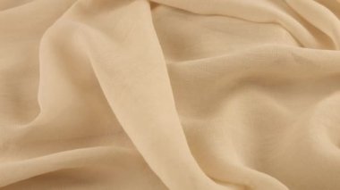 Dönen vitrindeki ince vanilyalı bej şifon kumaşın yumuşak kıvrımlarının yakın çekim görüntüsü. Moda, tasarım, kumaş teması üzerine aksesuar dikebilen tekstil arka planı.