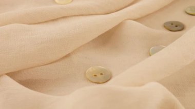 İnce badem bej rengi şifon kumaş ve doğal inci düğmelerinin yakın çekim görüntüsü. Moda temalı dikiş aksesuarları ile tekstil arka planı.