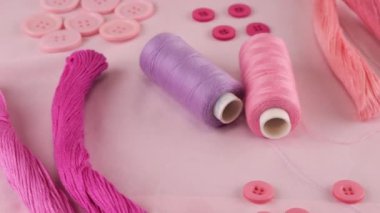 Pamuk kumaşın üst görüntüsü, düğmeler ve iplik makaraları, diş ipi, pembe rengin farklı tonlarında iplik. Tekstil arka planı vitrinde döner. Moda temasının arka planı.
