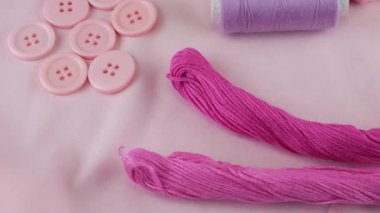 Pamuk kumaşın üst görüntüsü, düğmeler ve iplik makaraları, diş ipi, pembe rengin farklı tonlarında iplik. Tekstil arka planı vitrinde döner. Moda temasının arka planı.