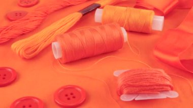 Mercan pembe pamuk kumaş, düğmeler ve iplik makaraları, diş ipi, turuncunun farklı tonlarında iplik. Tekstil arkaplanı görüntüleme kutusunda döner.