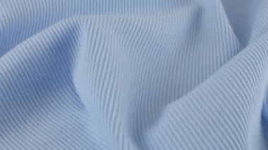 İnce açık mavi pamuklu formanın yumuşak kıvrımlarının üst görüntüsü. Tekstil arka planı vitrinde döner. Moda, tasarım, doğal kumaş teması üzerine arka plan.