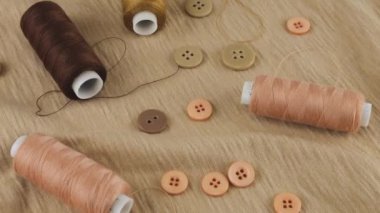 İnce bej renkli pamuk forma, düğmeler ve ipliklerin farklı tonlarda kahverengi ve pembe iplikler dönen bir vitrinde. Tasarım teması, moda, kıyafet terziliği. Üst görünüm.