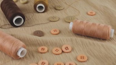 İnce bej renkli pamuk forma, düğmeler ve ipliklerin farklı tonlarda kahverengi ve pembe iplikler dönen bir vitrinde. Tasarım teması, moda, kıyafet terziliği. Üst görünüm.