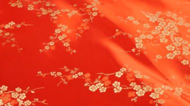 Şatafatlı kırmızı ipek kumaş arka planda çiçek desenli, doğu tarzı işlemeli, erik çiçeği desenli. Dönen bir vitrinde pırıl pırıl parlayan Brokar.