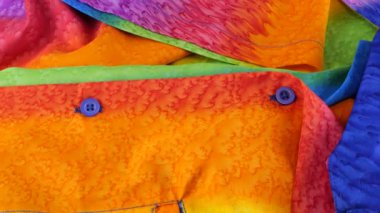 Gökkuşağı renklerine boyanmış parlak kumaştan yapılmış bir gömleğin üst görünümü bir vitrin üzerinde döner. Tasarım, moda, kıyafet ve aksesuar terziliği. LGBTQ temasının tekstil arkaplanı.