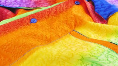 Gökkuşağı renklerine boyanmış parlak kumaştan yapılmış bir gömleğin üst görünümü bir vitrin üzerinde döner. Tasarım, moda, kıyafet ve aksesuar terziliği. LGBTQ temasının tekstil arkaplanı.